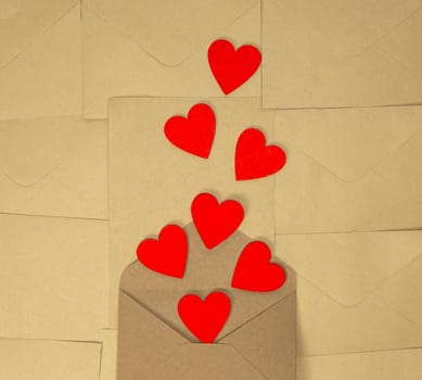 Valentines Day craft envelope with red hearts on brown plain paper background, Romantic love design top view, copy space beauty