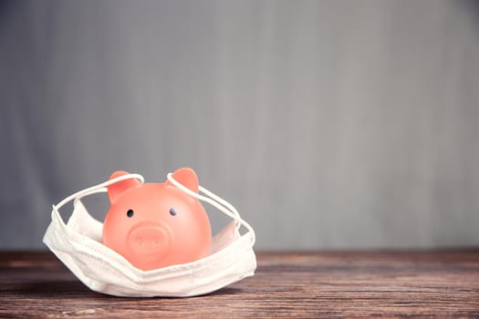 Inserting coin in piggy bank for savings with protective medical mask for pandemic, virus Covid-19, coronavirus,business,fianancial,saving concepy with copy space space for tect