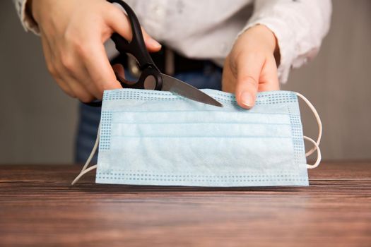 Young Female hands cut a medical mask with scissors, protective facial mask for Covid-19 ,Concept for ending the lockdown and coronavirus pandemic. vaccine