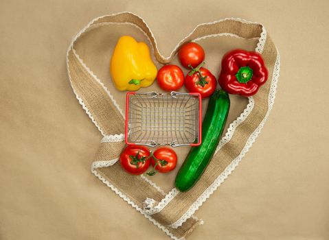 Fresh organic vegetables with a empty iron shopping basket surrounded with ribbon heart on brown craft paper top view, Health,vegetables,vegetarion concept copy space space for text