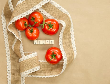 Vegan written with wooden cubes near fresh red tomatoes with brown craft paper background, surrounded with natural burlap ribbon, Vegan, Vegetarion, Healthy food concept copy space top view