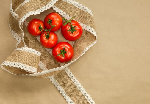 Red Tomatoes on brown craft paper background with natural colored burlap ribbon top view, copy space, Vegan, vegetarian,healthy food,vegetables concept space for text