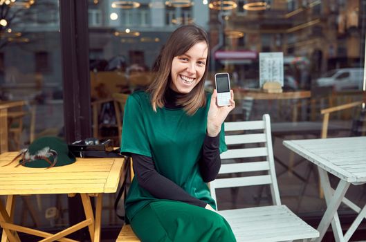 Portrait of cheerful young caucasian woman in green clothes that sitting outside cafe