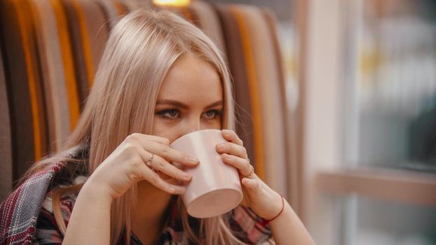 A young woman drinks coffee in cafe. Mid shot
