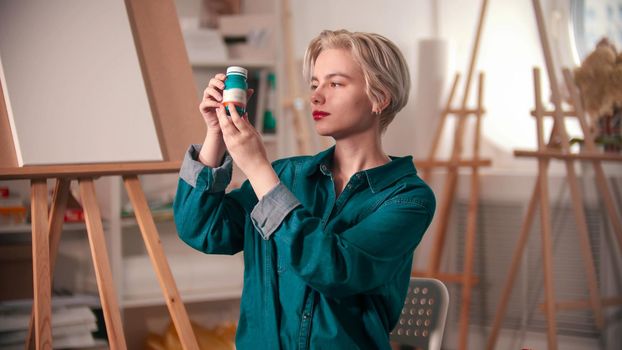 A young woman artist opening up a blue paint tube. Mid shot