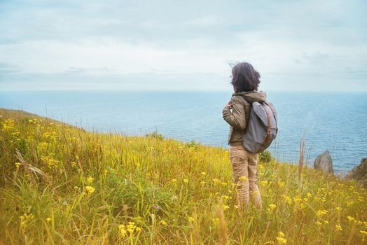 Hiker woman with backpack looks on the sea, rear view