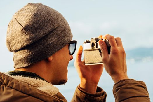 Traveler hipster young man takes photographs with vintage photo camera on coastline near the sea