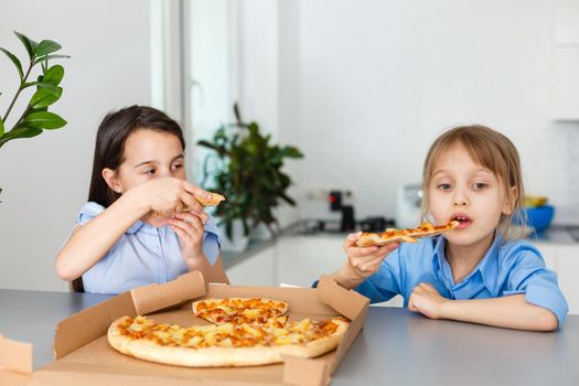 Two happy little child girl friends eating pizza slices.