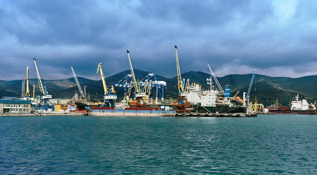 Seaport cargo crane in harbor on background of mountains and blue sky. Space for text in low part of image