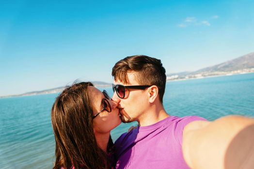 Happy young couple in love kissing and taking self-portrait on beach on background of blue sea