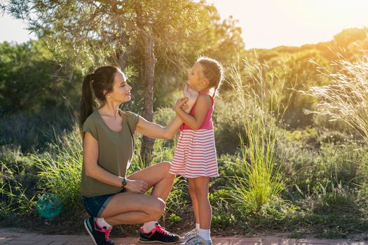 Beautiful mother and her little daughter outdoors. Beauty Mum and her Child sitting on Park pathway together at sunset. Outdoor Portrait of happy family. Mother's Day.