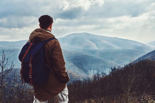 Hiker man with backpack looking at the mountains at autumn season, rear view. Low contrast effect