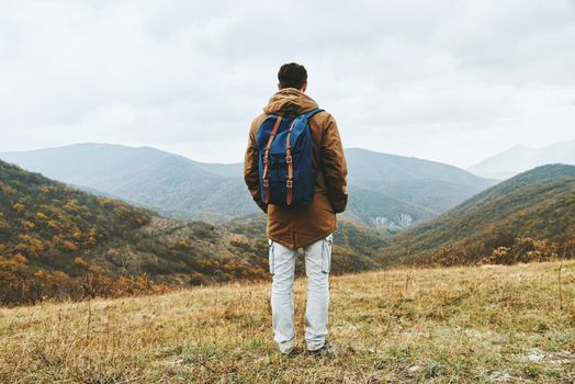 Hiker man with backpack in full length standing among mountains and enjoying by scenics in autumn season