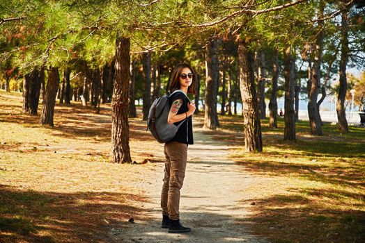 Hipster young woman walking in pine tree park at sunny day