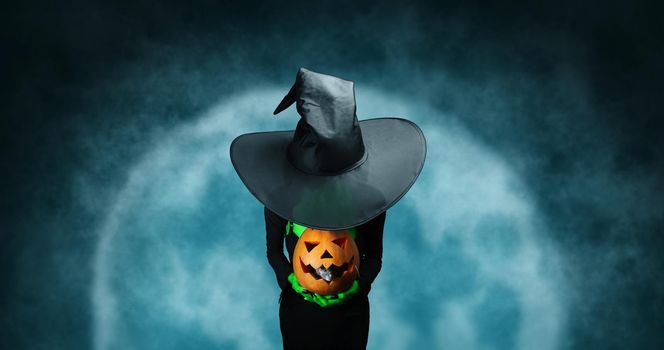 Mystery Halloween witch holds carved pumpkin on full moon background. Halloween, horror theme