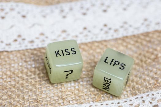 Two erotic dice for sexual game with cotton lace background texture, with the text Kiss lips for Valentines Day,sex,sensual,romantic, love concept close up
