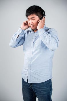 Love this music. Handsome young man in headphones holding mobile phone and smiling while standing against grey background