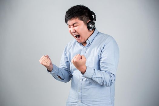 Love this music. Handsome young man in headphones holding mobile phone and smiling while standing against grey background