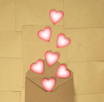 Paper craft envelope with pink hearts on brown plain background. Concept of love and Valentines Day, top view copy space. Romantic design