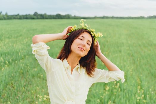 Smiling beautiful young woman with wreath of flowers enjoying a summer day
