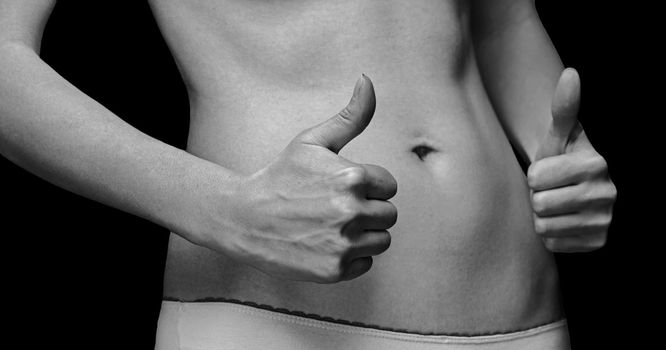 Woman with gesture sign thumb up in front of her slim abdomen, monochrome image
