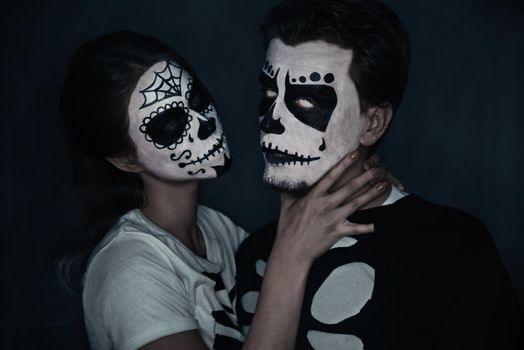 Halloween loving couple in costumes of skeletons and skull makeup. Woman strangles a man