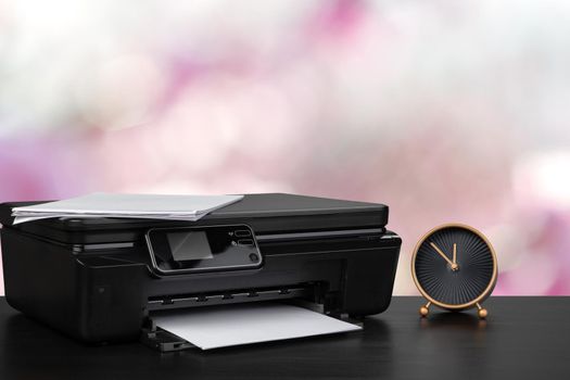 Compact laser printer on black desk against blurred background, close up