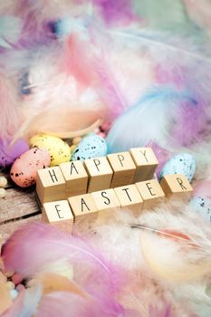Happy Easter written with wooden cubes surrounded with beautiful pastel colored decorative feathers and eggs, April, Easter, Religion, Spring concept for background and greeting card top view bright colors