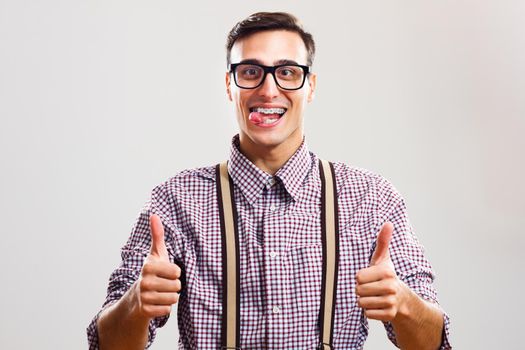 Portrait of nerdy man giving thumb up and sticking out tongue