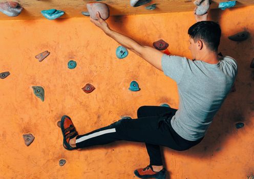 Young man climbing up on wall in gym, side view