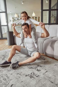 Happy father is doing training indoors and playing with little girl on couch in living room