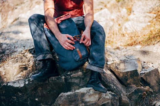 Unrecognizable hiker man opening his backpack on nature. Hiking and recreation theme