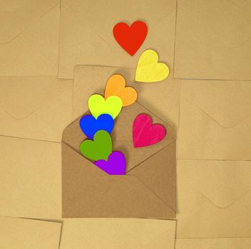 Brown craft paper envelope with various rainbow colorful hearts on plain brown background texture top view, Valentines Day, romantic concept copy space love