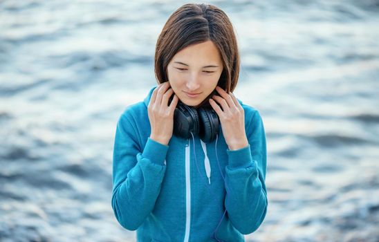 Young beautiful woman with big headphones walking on coast