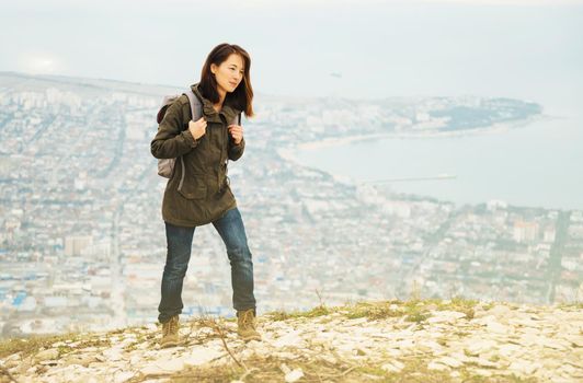 Young traveler woman with backpack walking in highlands over the city. Hiking and recreation theme