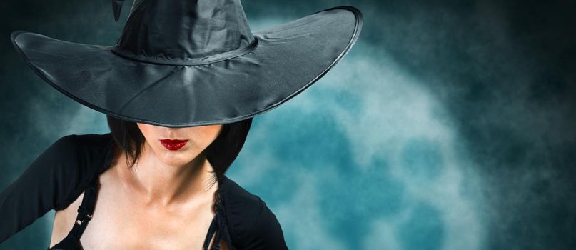 Beautiful fashionable witch in black hat and dress on background of full moon. Halloween theme