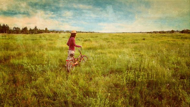 Hipster girl in straw hat walking with bicycle on summer meadow outdoor. Vintage image