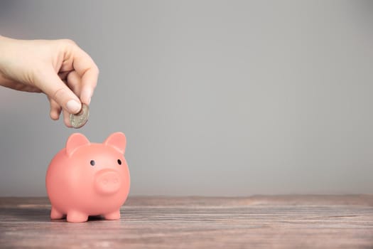 Human Hand Putting Coin In pink Piggy Bank on blurred background, Saving, business,financial concept copy space retro modern design