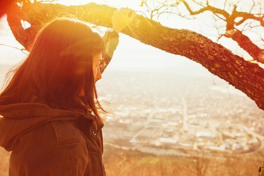 Traveler young woman looking at the city from hill. Concept of tranquil life from the urban bustle. Image with sunlight effect