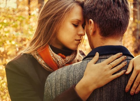 Young beautiful blond woman embraces a man in autumn park, tenderness scene