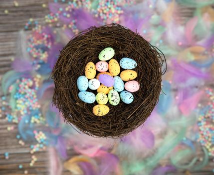 Colorful Easter eggs in bird nest surrounded with pastel colored feathers and wooden cubes with the text Happy Easter top view, modern background design, Easter holliday, Spring, concept greeting card