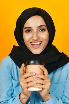 woman in black hijab glass with a drink emotion relaxation yellow background. High quality photo