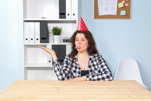 Portrait of pleased happy young woman with funny cone on head and in white jacket smiling at camera, enjoying birthday party, holiday celebration. indoor studio shot isolated on blue background