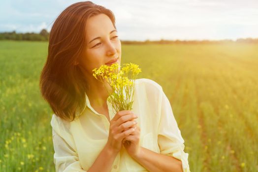 Smiling beautiful young woman holding bouquet of yellow flowers in summer outdoor. Image with sunlight effect