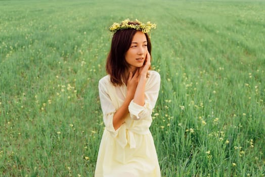 Beautiful brunette young woman with wreath of flowers resting on summer meadow