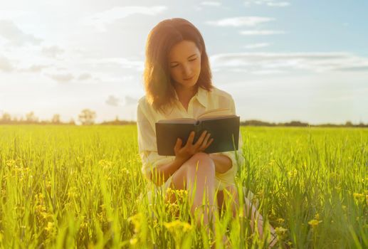 Beautiful young woman reading a book on summer meadow. Image with sunlight effect
