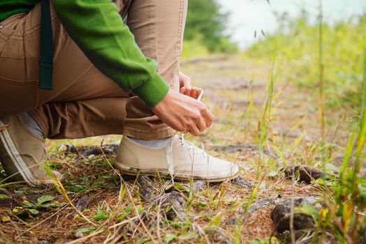 Hiker woman tying a shoelaces in summer forest, face is not visible