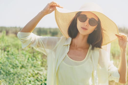 Beautiful young woman in sunglasses and hat with wide brim resting in summer park