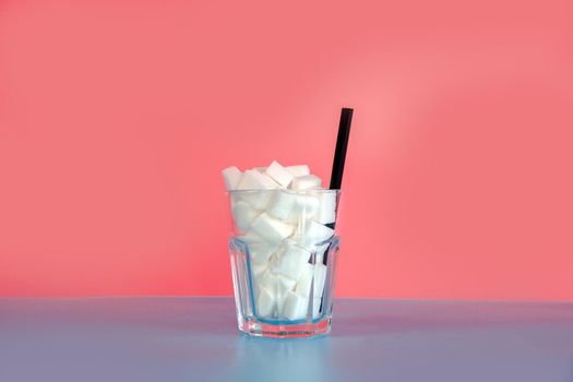 Glass full with sugar cubes with straw on pastel pink and blue background with copy space, retro design, Sweets,candy,soda,unhealthy eating concept. modern design colorful
