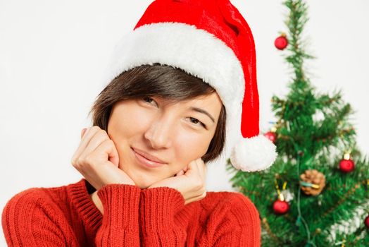 Portrait of a beautiful woman in a santa hat on a background of Christmas tree
